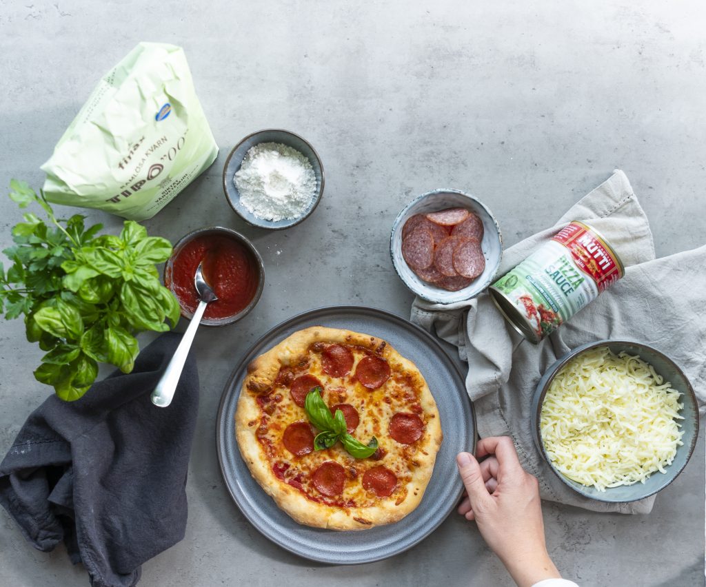 Köksbänk med peperonipizza och ost, tomatsås och öret i olika skålar